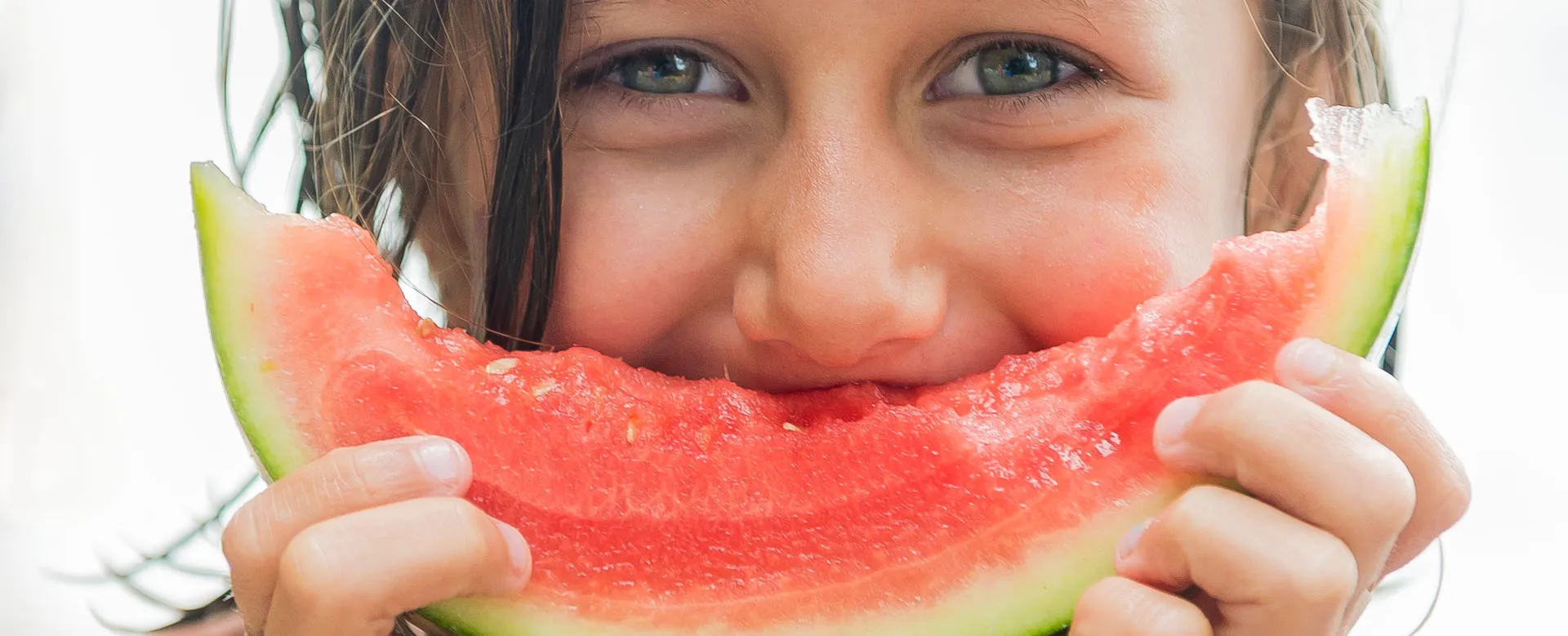A child grinning behind a big slice of watermelon